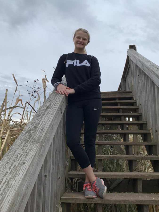 Kamryn Litchas poses on the Valas corn maze bridge with a beautiful smile. She is expressing the normal outfit for most teens with tennis shoes, black leggings, a black sweatshirt, and a handy little black bag.