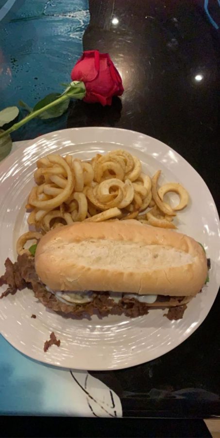 A cheesesteak philly with curly fries and a red rose.