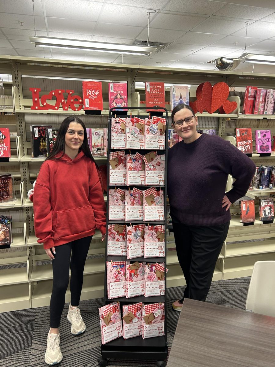 Sophomore student aide Callie Thompson and librarian Carmen Anderson pose next to the Valentine's Day Speed Dating display.